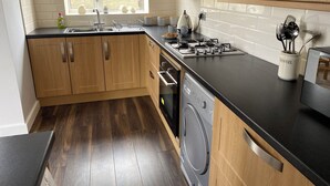 A modern kitchen with wooden cabinets, a black countertop, a gas stove, a dishwasher, and a window with a view of the outside.