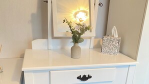 A white vanity with a mirror, a vase with flowers, a tissue box, and a bench.