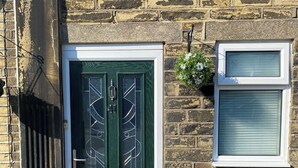 A green double door with a white frame, a small window with a white frame, and a stone wall.