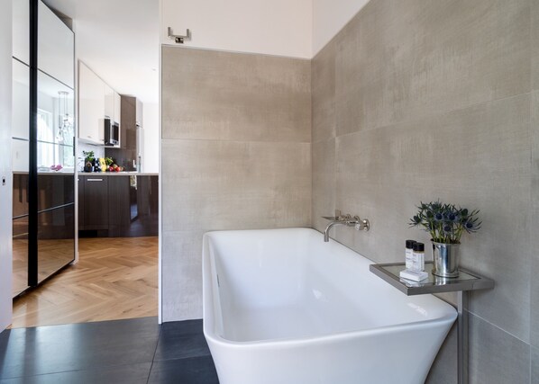 A modern bathroom with a freestanding bathtub, a glass shower enclosure, and a small shelf with toiletries.