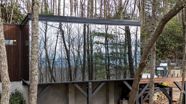 A modern cabin with a large window overlooking a forest.