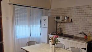 A compact kitchen with a refrigerator, microwave, and a small countertop. There is a dining table with chairs and a vase with flowers. - CASA CHALET LAMAR (whole house) (Santa Clara del Mar)