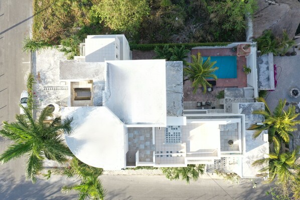 Vista aérea de una casa moderna con piscina, rodeada de palmeras.