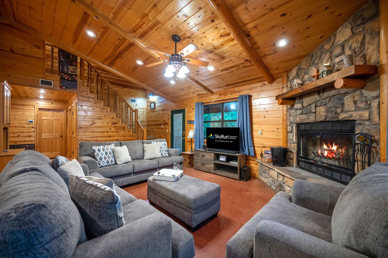 L’intérieur d’un chalet confortable, avec une cheminée en pierre, un grand canapé, un téléviseur et un escalier.