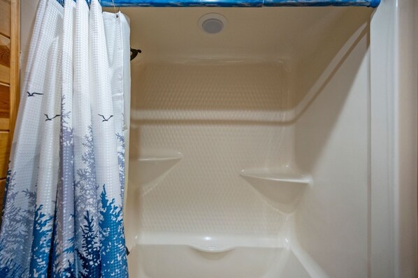 Un baño con cortina de ducha con estampado de pájaros y copos de nieve, una bañera blanca y un lavamanos blanco.