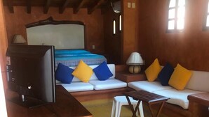 A cozy room with a bed, a TV, a small table, and a sofa. - Villa Soleil (Zihuatanejo)