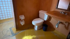 A bathroom with a white toilet, a sink, and a mirror. - Villa Soleil (Zihuatanejo)
