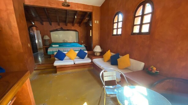 A room with a bed, a sofa, a glass table, and a chair. - Villa Soleil (Zihuatanejo)