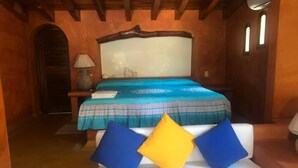 A bedroom with a bed, a nightstand, a lamp, and a window. - Villa Soleil (Zihuatanejo)