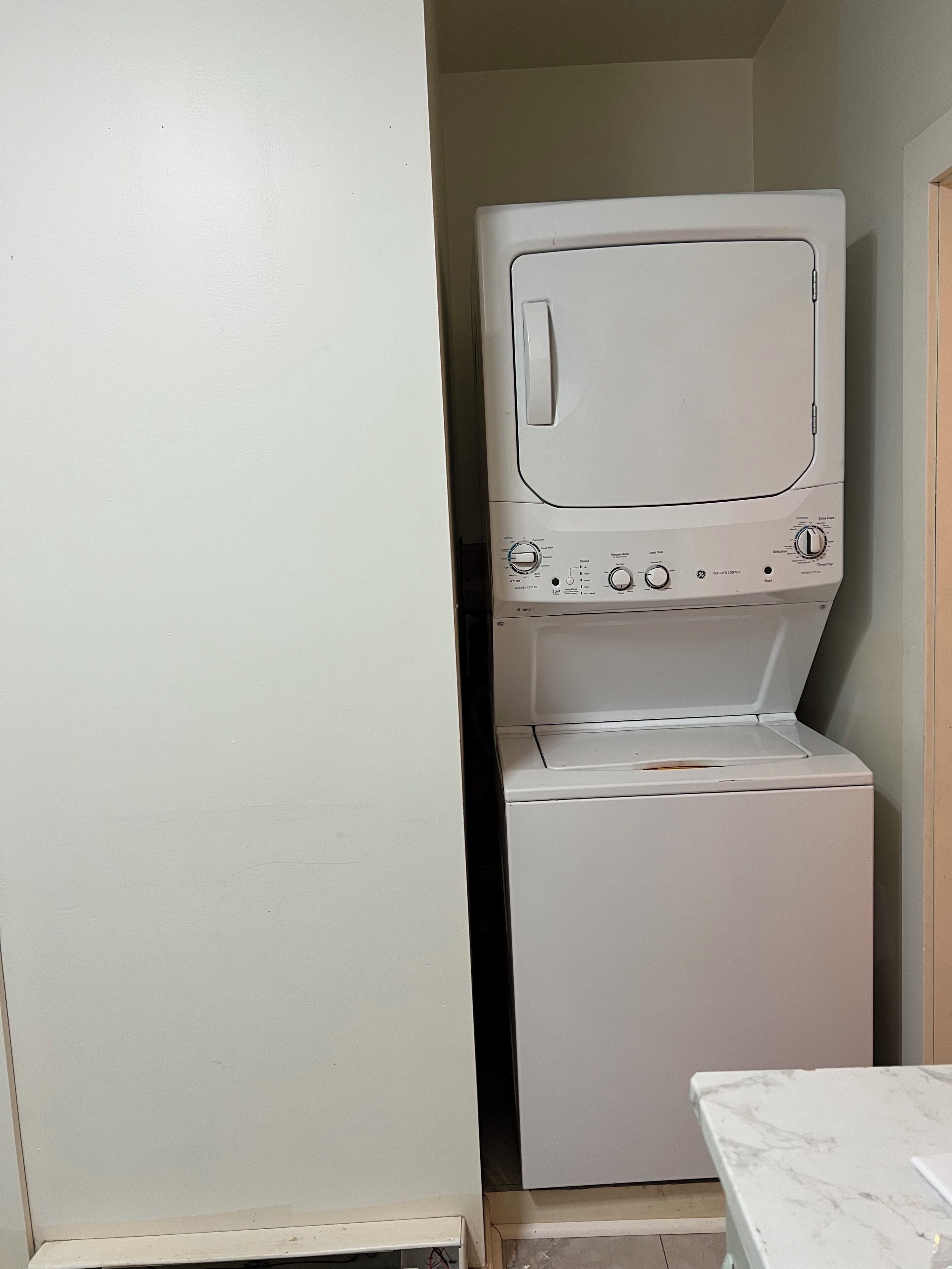 A compact laundry room with a front-loading washer and dryer, a small table, and a door leading to another room.