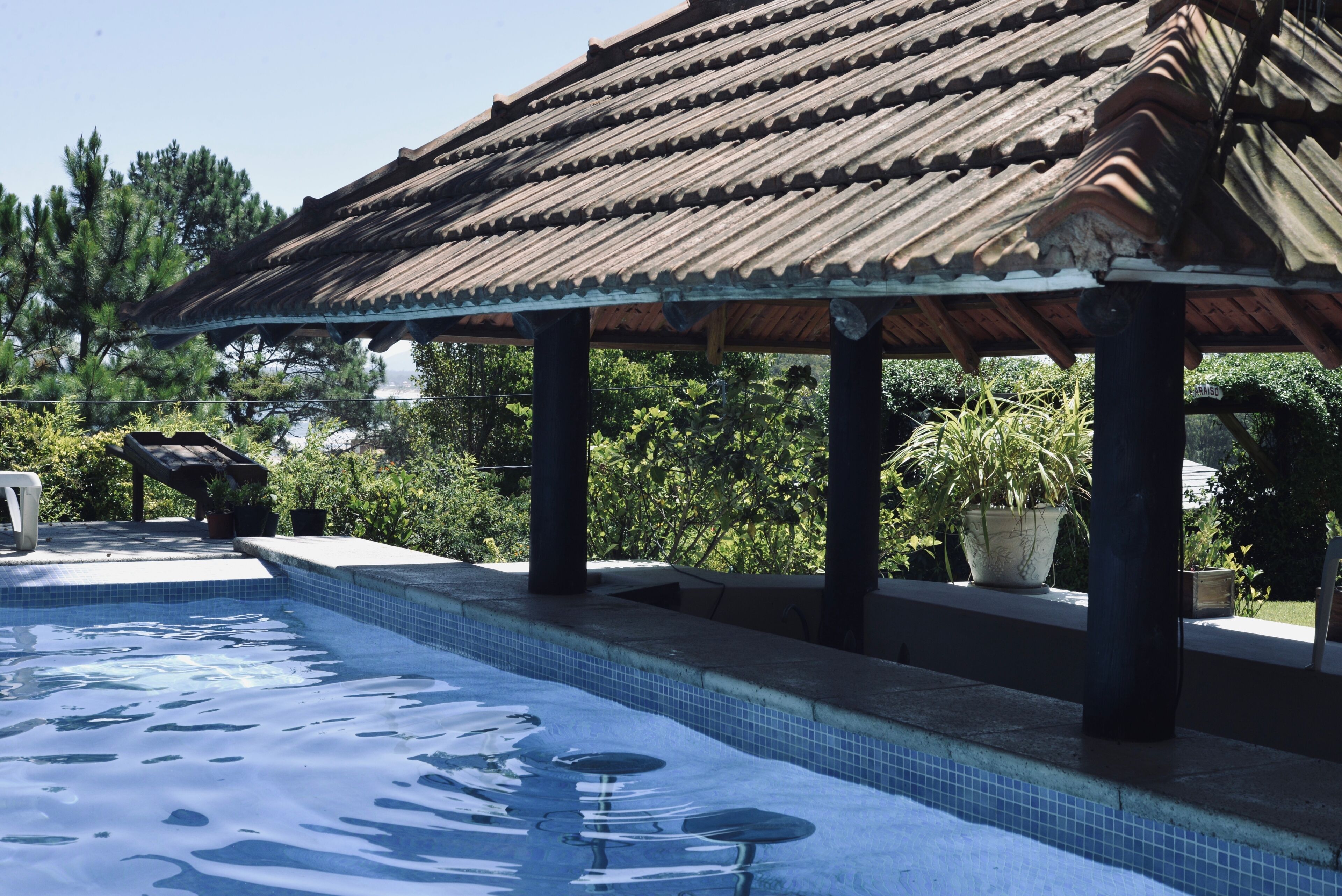 Piscina con solárium empedrado y zona cubierta con techo de azulejos.