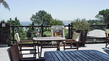 An outdoor seating area with wooden tables and chairs, a sign with a warning, and a view of the sea.