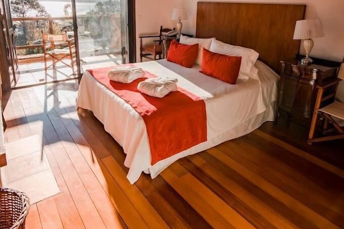 Un dormitorio con una cama grande, suelo de madera y vistas a través de un ventanal.