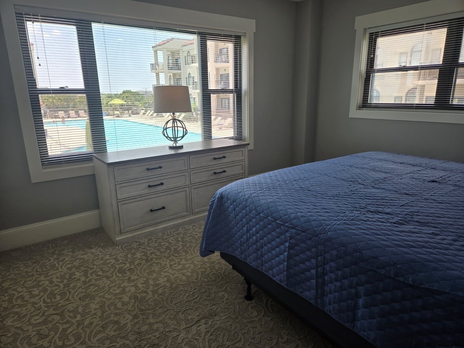 A bedroom with a bed, a dresser, and a window with blinds.
