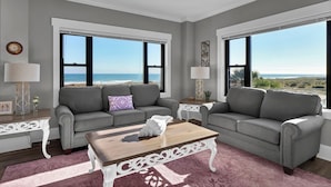 A living room with two grey sofas, a wooden coffee table, and a view of the ocean. - Wrightsville Oceanfront Condo: Pool, Ocean Views, Beach Access (Wrightsville Beach)