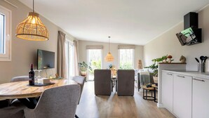 A modern kitchen with white cabinets, a wooden dining table, and a hanging light fixture.
