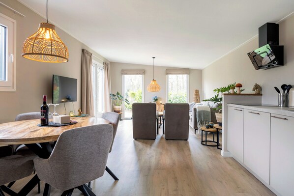 A modern kitchen with white cabinets, a wooden dining table, and a hanging light fixture.