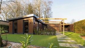A modern house with a glass door entrance, a covered patio, and a well-maintained lawn.