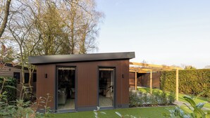 A modern house with a glass door entrance, a wooden exterior, and a well-maintained garden with artificial grass and plants.