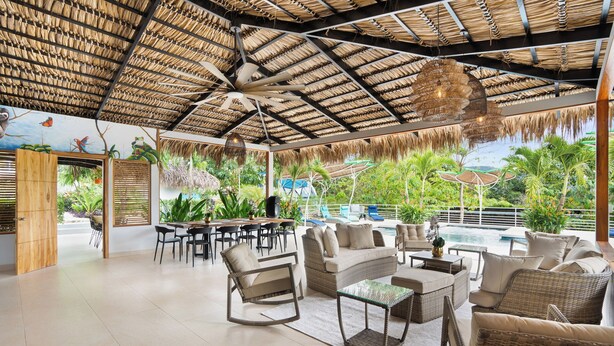 A spacious outdoor lounge area with wicker furniture, a pool, and a thatched roof. - Family Villa w Resort-Style Pool - 5 Min to Beaches (Potrero)