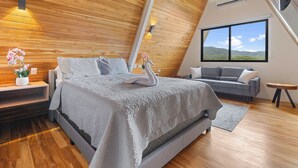 A modern bedroom with a wooden ceiling, a large bed with a swan-shaped pillow, a gray sofa, and a view of the outdoors. - Family Villa w Resort-Style Pool - 5 Min to Beaches (Potrero)