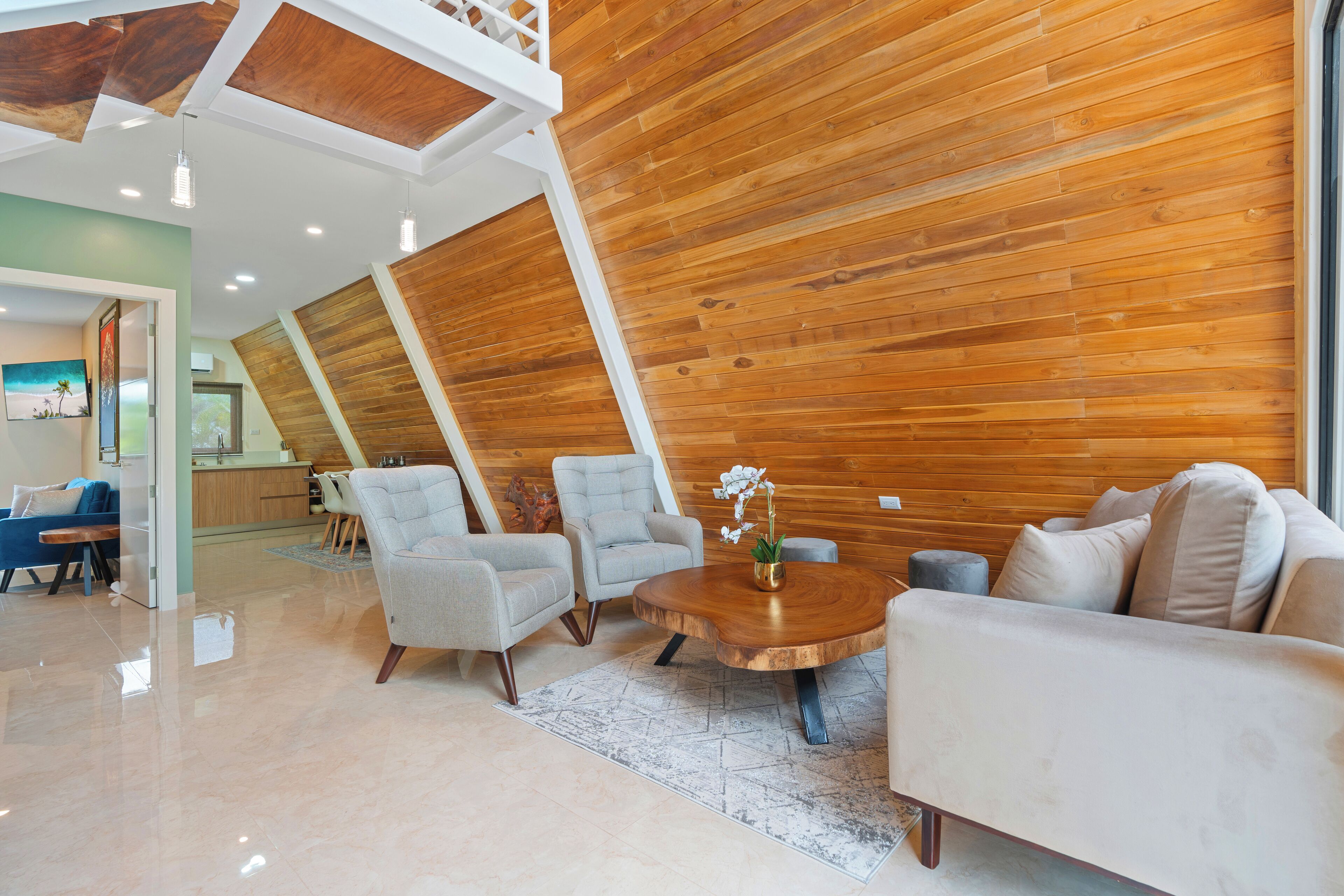 Un interior moderno con techo inclinado de madera, una mesa de centro redonda de madera y un sofá beige.