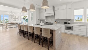 A modern kitchen with white cabinetry, a large island with bar stools, pendant lighting, and a view of the outdoors. - Bikes, Close Beach Access, Gulf View, Private Pool (Inlet Beach)