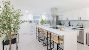 Una cocina moderna con armarios blancos, un refrigerador de acero inoxidable y una isla central con taburetes de bar.