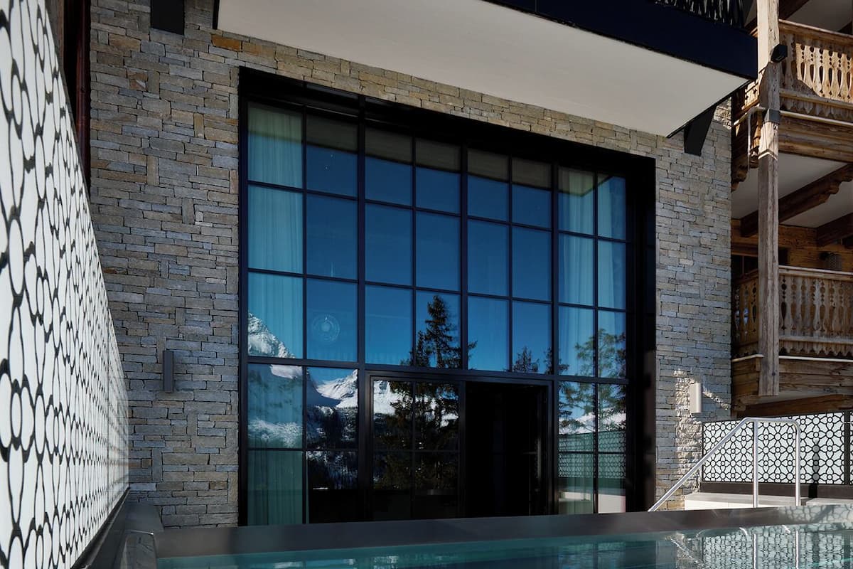 A modern indoor swimming pool with a glass wall reflecting a snowy mountain landscape.