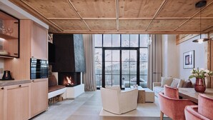 Ein modernes Wohnzimmer mit Kamin, Holzboden und großen Fenstern mit Blick auf die Berge.