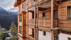Ein mehrgeschossiges Holzhaus mit Balkonen vor einer gebirgigen Kulisse.