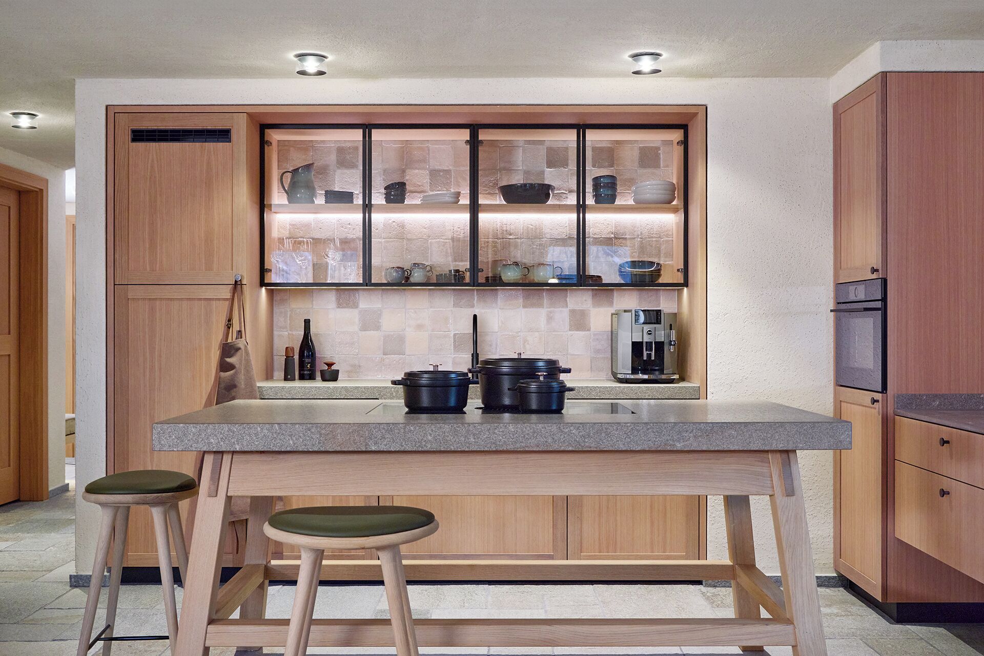 Een moderne keuken met houten kastjes, een granieten aanrecht en twee barstoelen.