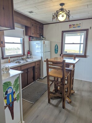 Une cuisine avec des meubles de rangement en bois, un réfrigérateur blanc, une table à manger en bois avec des chaises, une fenêtre avec vue et un luminaire suspendu.