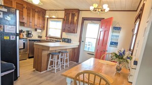 Una cocina con armarios de madera, una isla central con taburetes, una mesa de comedor con sillas, un refrigerador y un lavamanos.