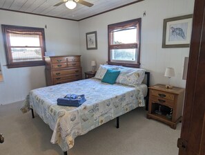 A bedroom with a bed, two nightstands, a dresser, two windows, and framed artwork on the walls.
