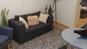Ein modernes Wohnzimmer mit einem dunklen Sofa, einem runden Couchtisch und einem gemusterten Teppich.