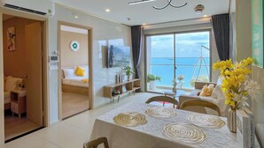 A modern hotel room with a balcony, a dining area with a table set for two, and a television mounted on the wall. - OLIU'S HOMESTAY - The Sóng Vũng Tàu (Ho Chi Minh City)