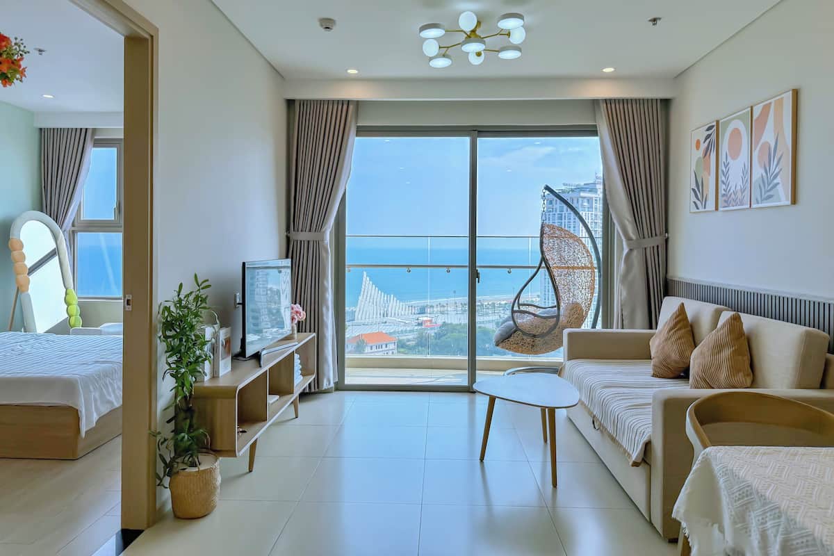 Une chambre d’hôtel moderne dotée d’un balcon, d’un fauteuil suspendu, d’un canapé, d’une télévision et d’une plante en pot.