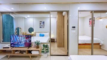A modern hotel room with a bed, a desk with a computer, a television, and a small plant.