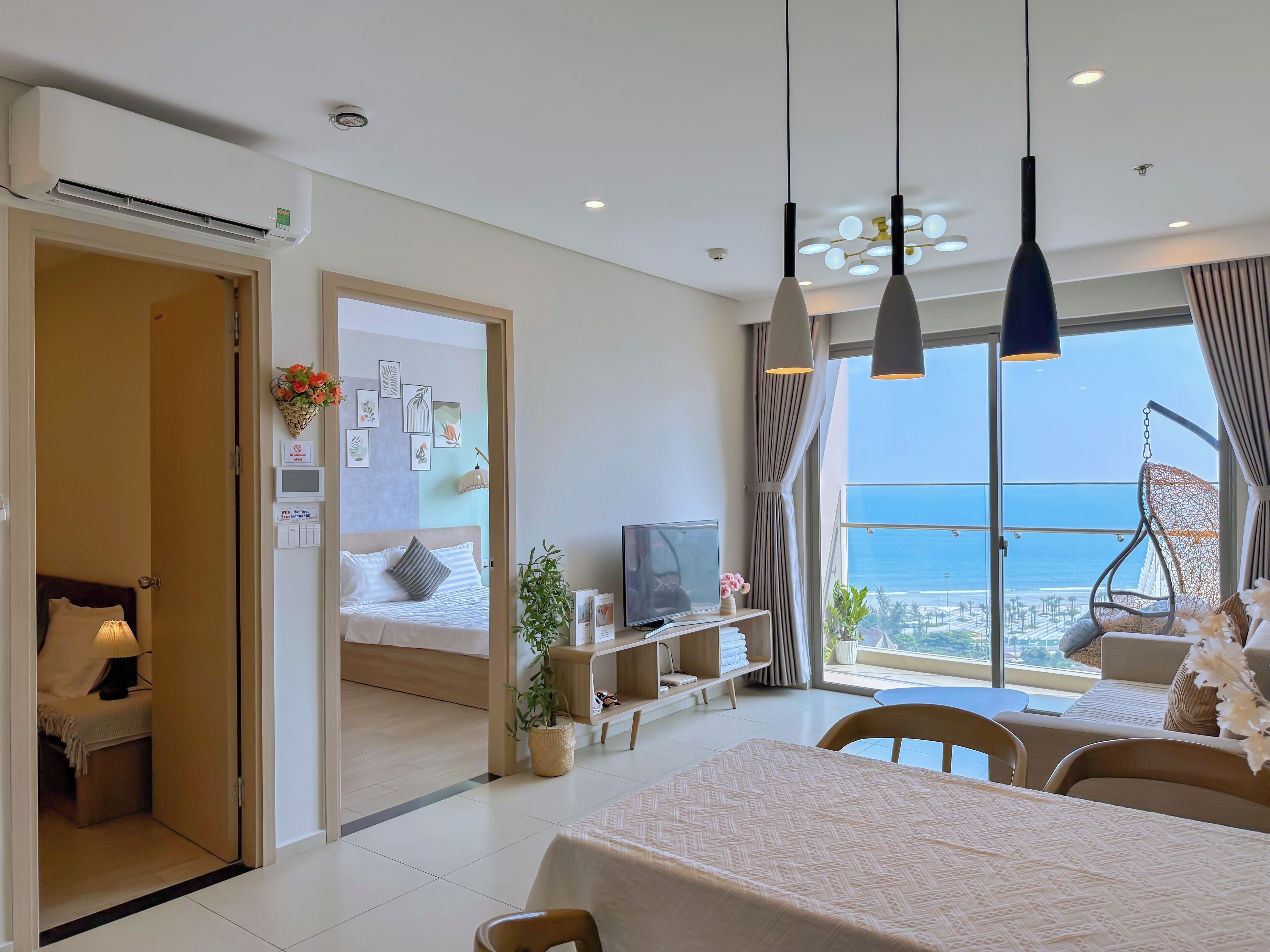 A modern hotel room with a bed, a TV, a dining area, and a balcony with a view of the sea.