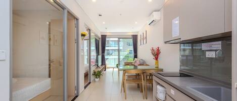 A modern kitchen with a dining area, a glass door leading to a balcony, and a small seating area with a bed.