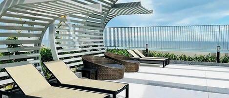 A rooftop terrace with lounge chairs, a pergola, and a view of the ocean.