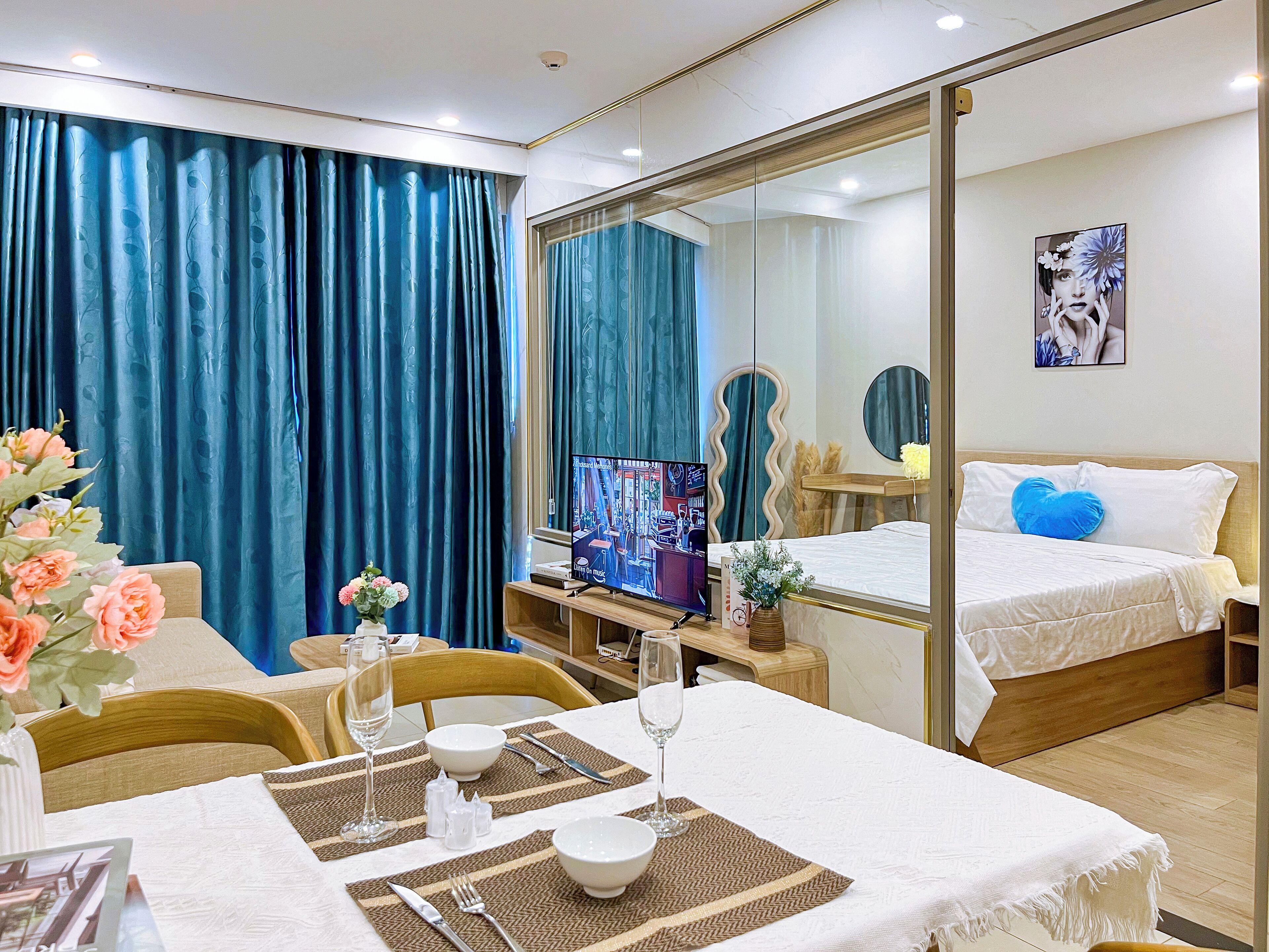 Habitación de hotel con cama, televisor, mesa de comedor para dos personas y un amplio ventanal con cortinas.