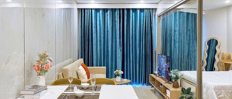 A hotel room with a dining area, a bed, a TV, and a large window with curtains.