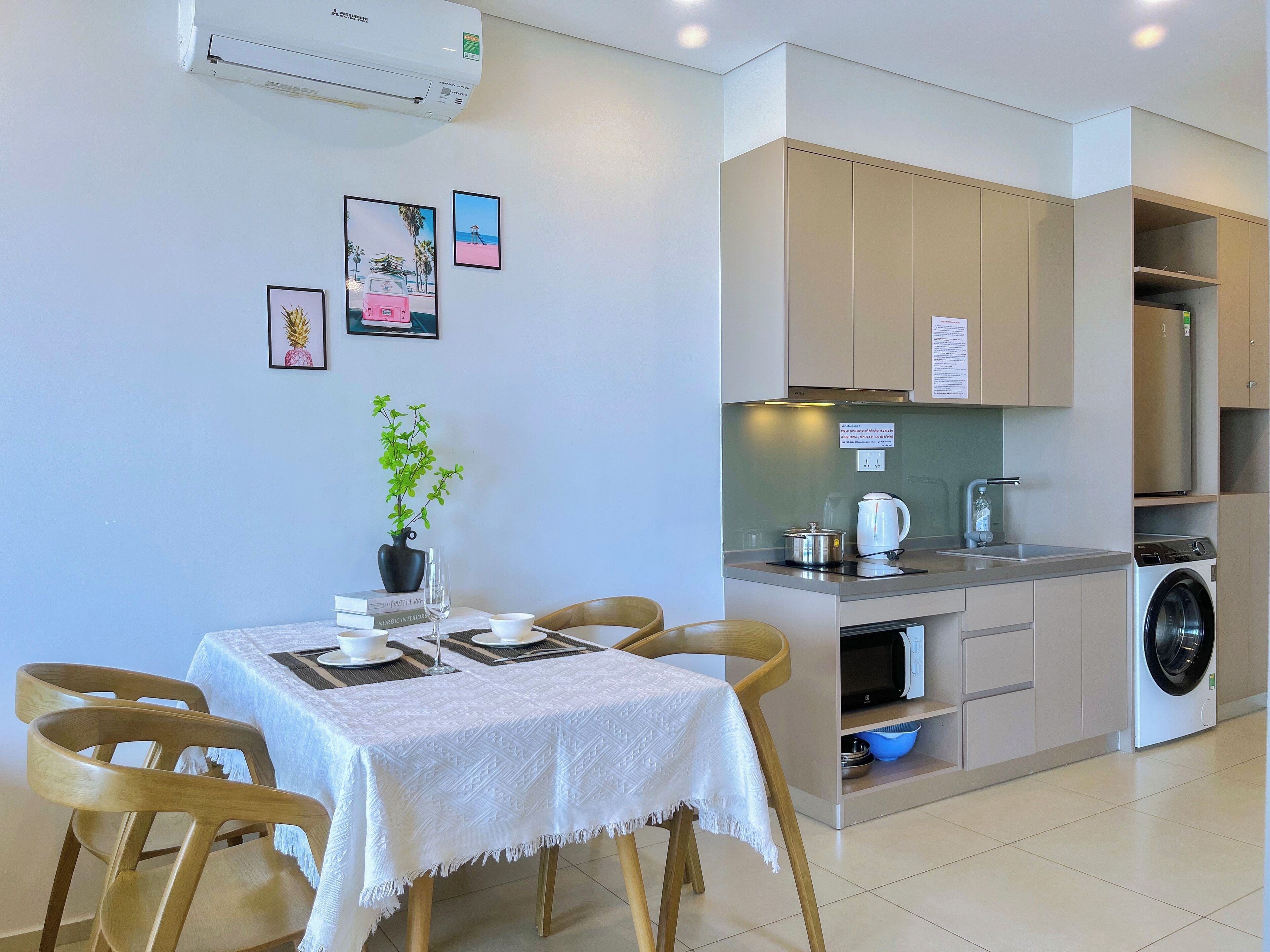 A modern kitchen with a built-in washing machine, a dining area with a table set for two, and a small potted plant.