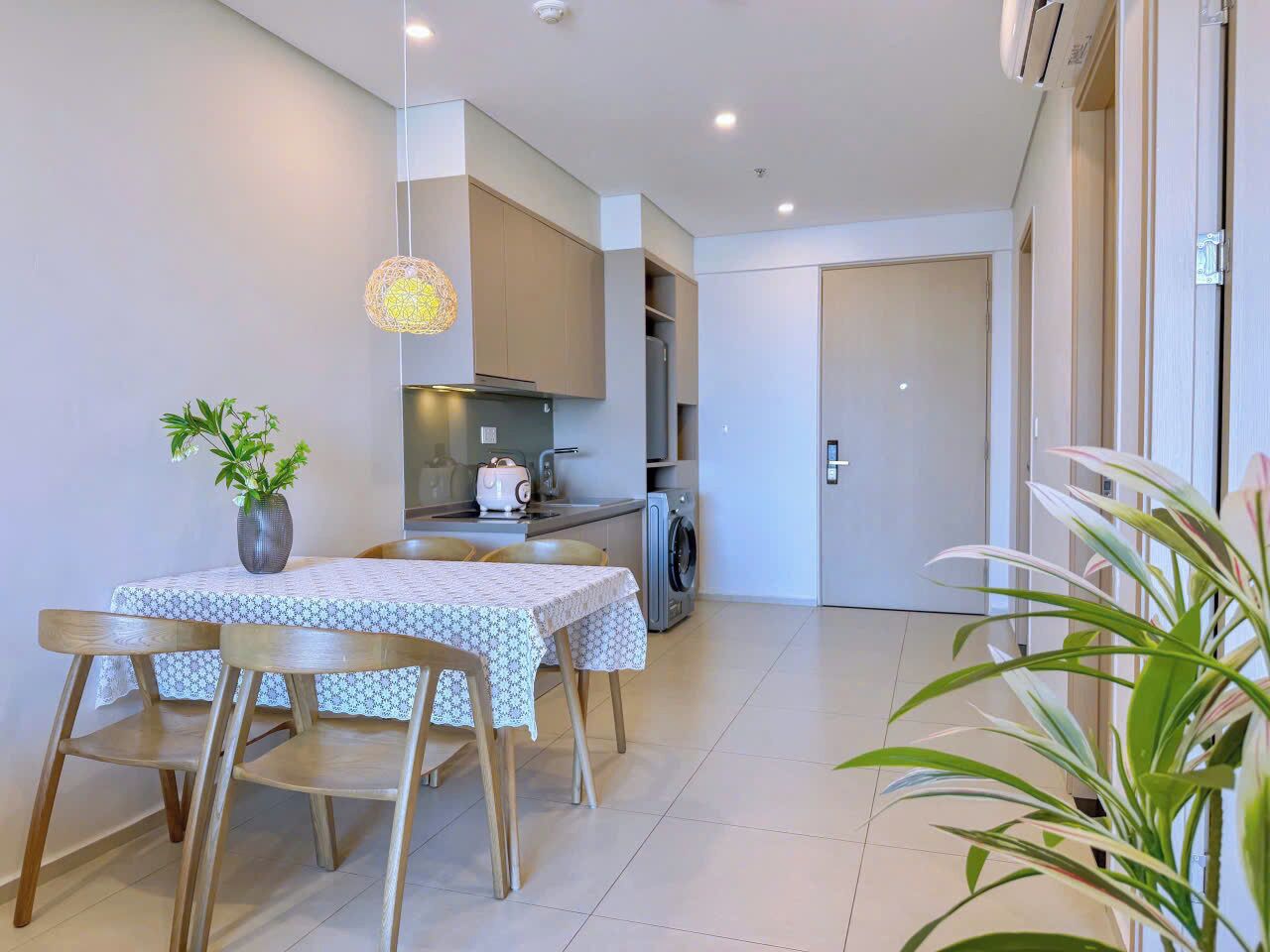 A modern kitchen with a dining area, including a table with chairs, a hanging light fixture, and a potted plant.
