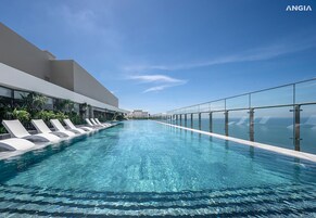 Una piscina infinita moderna con agua azul cristalina, rodeada de sillones blancos y palmeras, con vista a un cielo despejado.