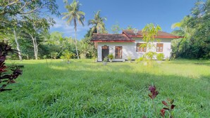 A white building with a red roof, surrounded by lush greenery and palm trees. - Riverside Nature Haven Villa  (weligama)