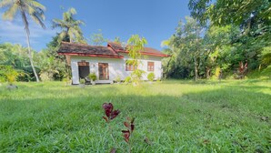 A house with a red-tiled roof and white walls, surrounded by lush greenery and palm trees. - Riverside Nature Haven Villa  (weligama)