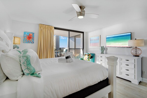 A hotel room with a bed, a ceiling fan, a window with a view of buildings, a TV, and a dresser. - Mainsail 472 - Gulf Front Condo, Community Pool, Hot Tub, Free Beach Service! (Miramar Beach)